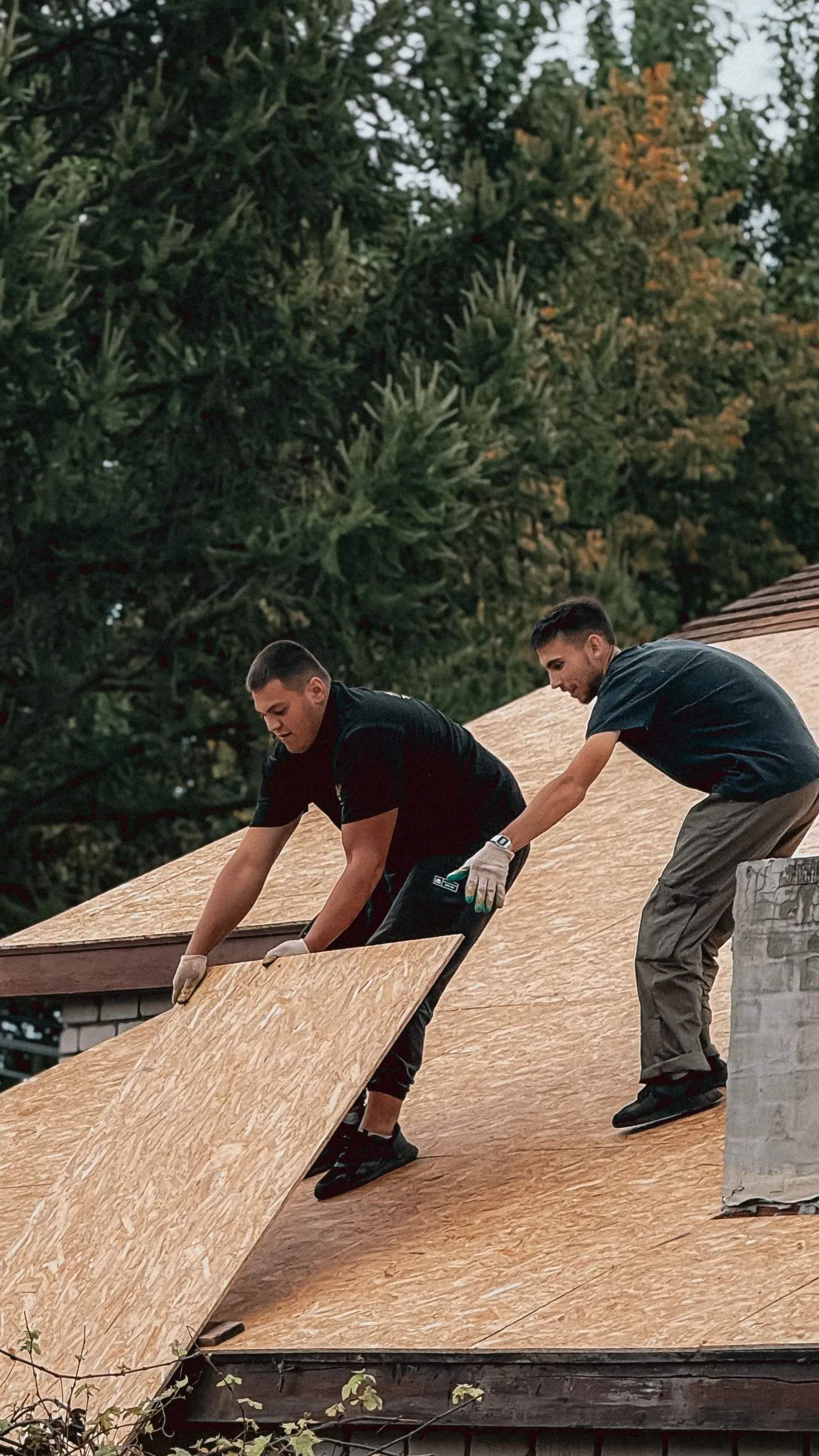 Two roofing crew members working together along the edge of a residential roof