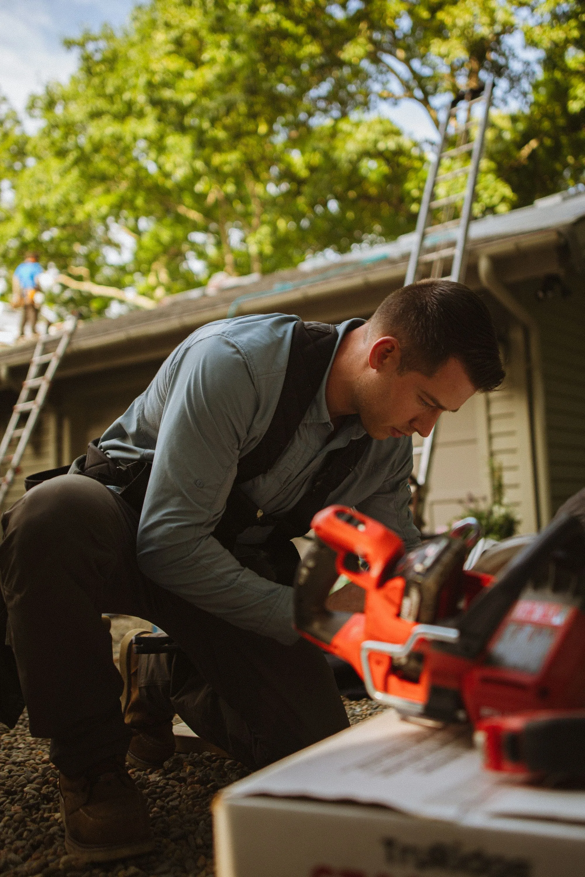 A roofing contractor working with a power tool at the side of a house
