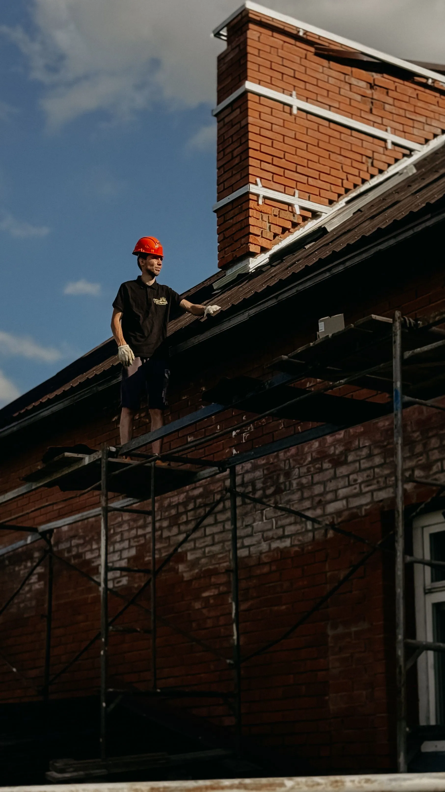 A roofer standing at the edge of a residential roof carrying out a shingle repair