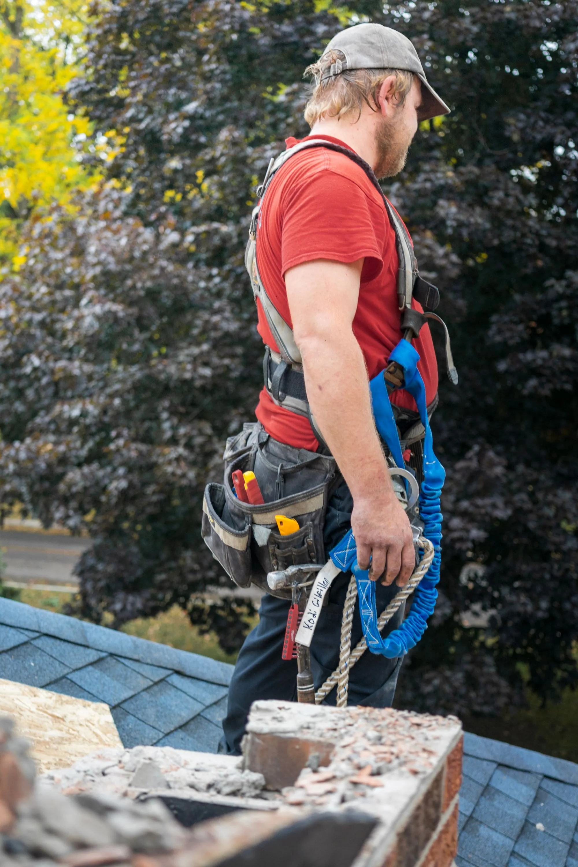 A roofer in a tool belt and harness preparing to work on a residential roof replacement