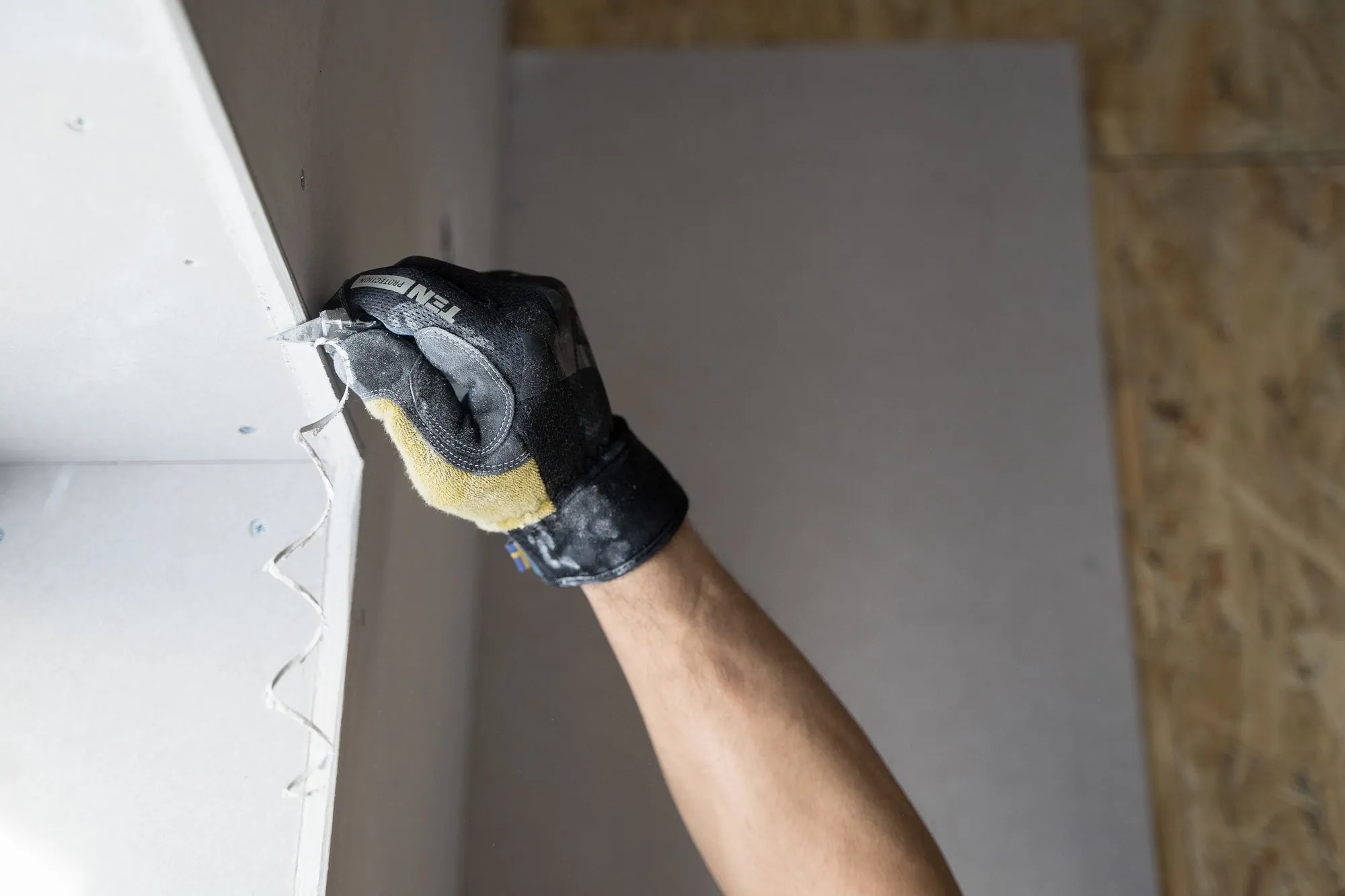 A worker in gloves fitting a new siding panel to the exterior wall of a house