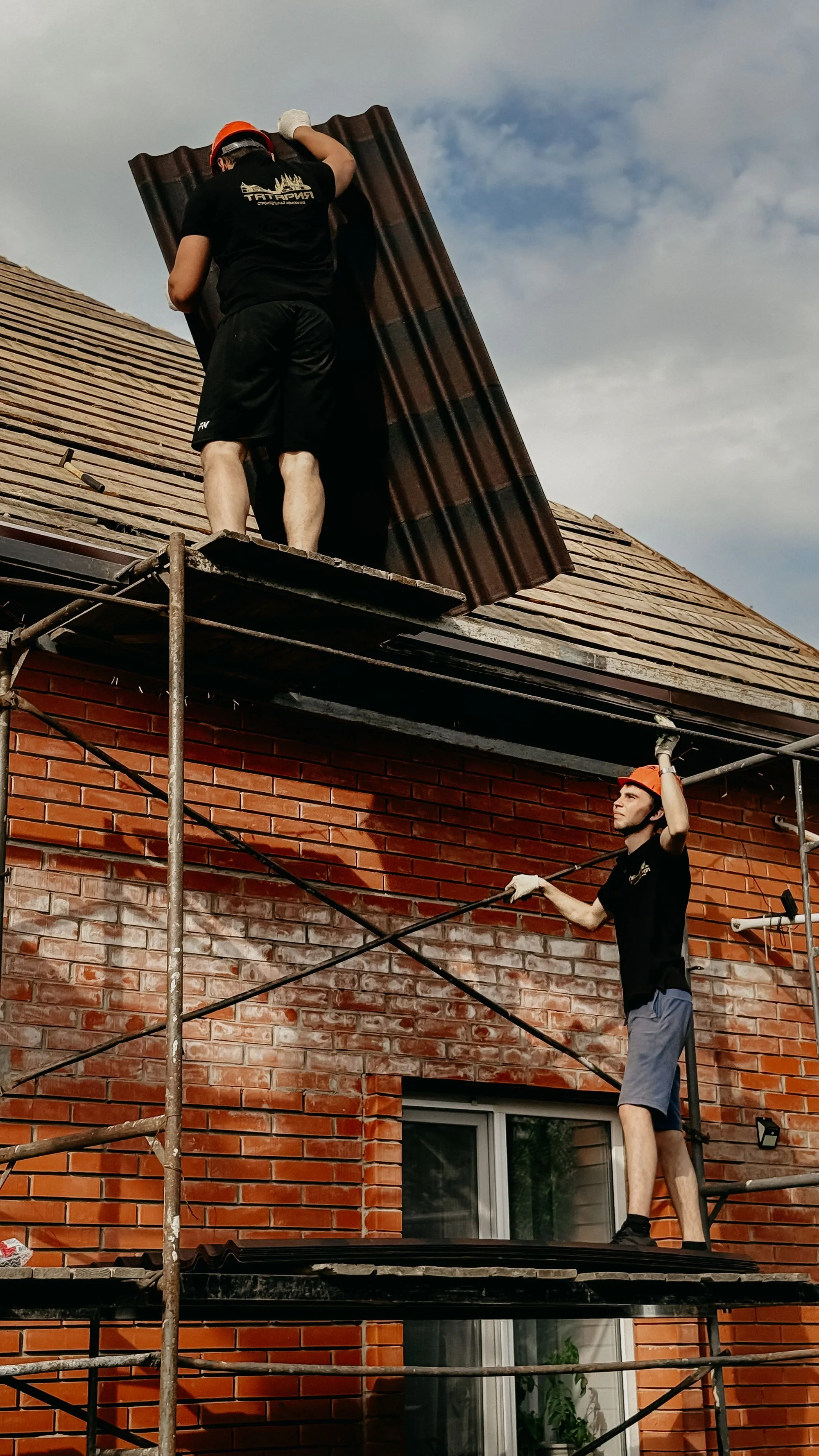 A roofer repairing damaged roof structure beneath the eaves of a house