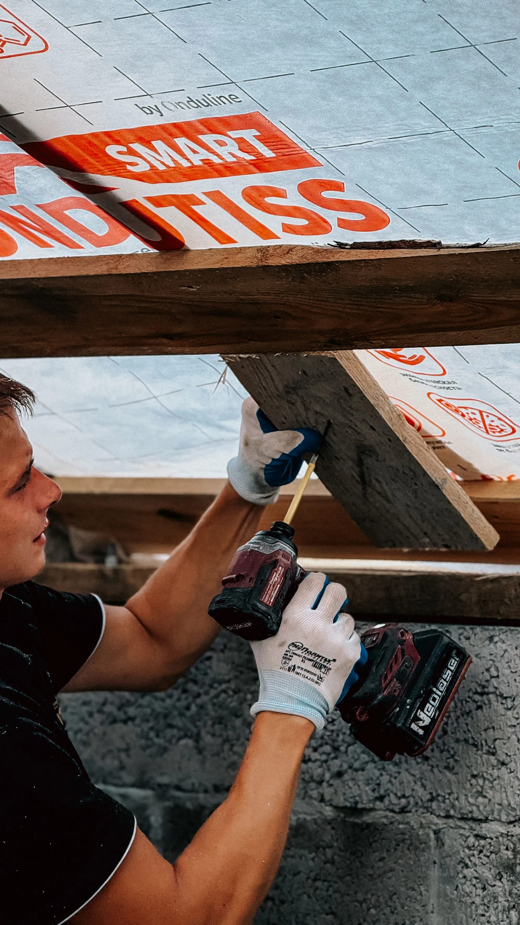 A roofer driving a fastener into a new roof board with a cordless drill